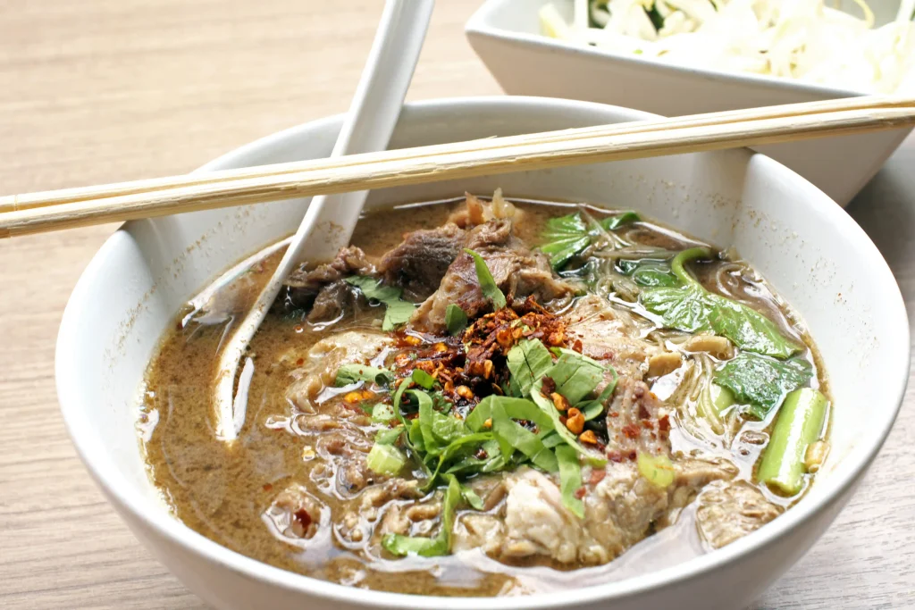 Thai Boat Noodle Garnished with Fresh Greens Veggies and Chili flakes