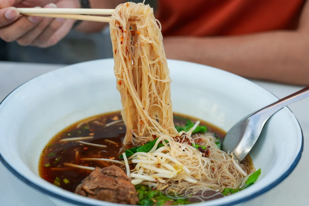 Person enjoying noodle and broth with chopsticks